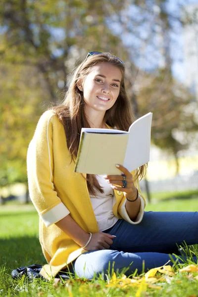 Mooie schoolmeisje in herfst park zitten en lezen van een boek — Stockfoto