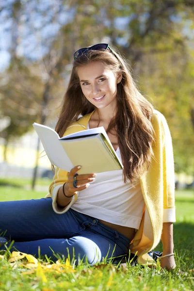 Mooie schoolmeisje in herfst park zitten en lezen van een boek — Stockfoto