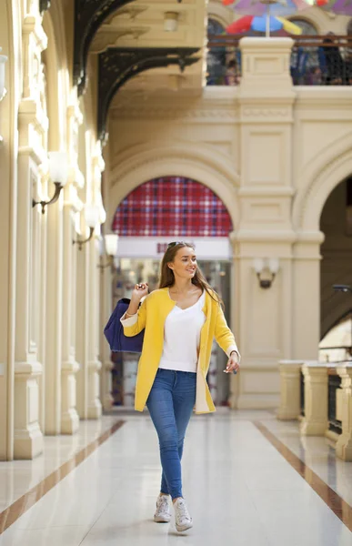 Mujer joven con abrigo amarillo caminando en la tienda — Foto de Stock