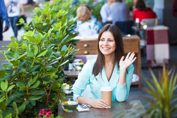 Woman sitting in a cafe welcomes waving her hand — Stock Photo, Image