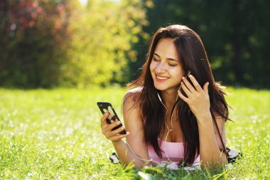 Elbiseli genç kadın yeşil çimenlerin üzerinde yatıyor ve müzik dinler