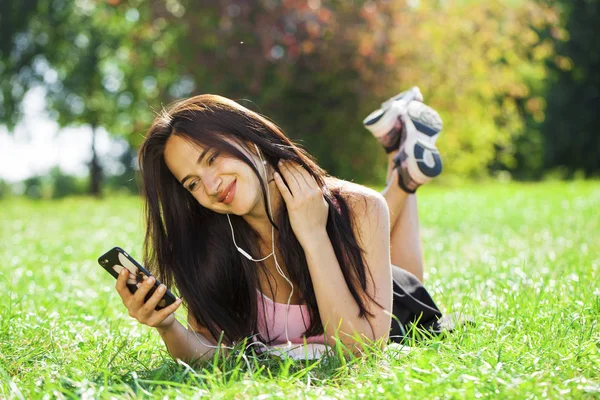 Jonge vrouw in jurk ligt op het groene gras en luistert naar muziek in — Stockfoto