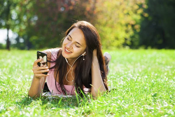Junge Frau im Kleid liegt auf grünem Gras und hört Musik in — Stockfoto