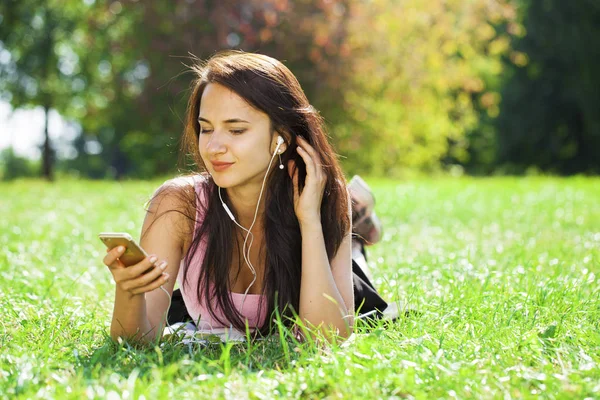 Mujer joven en vestido se encuentra en la hierba verde y escucha música en —  Fotos de Stock