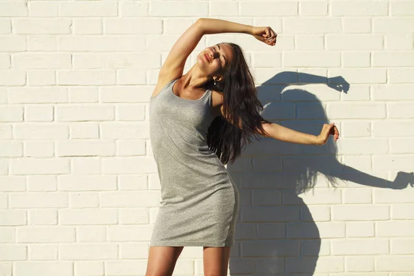 Beautiful young woman in sexy gray dress, against white wall — Stock Photo, Image