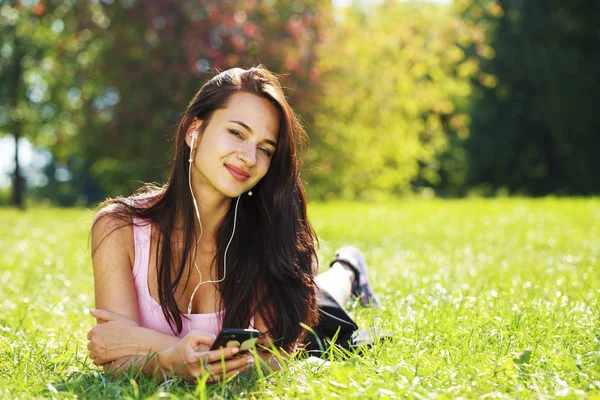 Jovem mulher de vestido encontra-se na grama verde e ouve música em — Fotografia de Stock