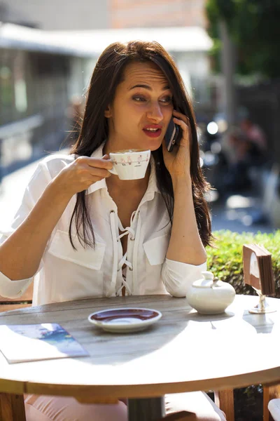 Elegant girl calling someone while resting in outdoor cafe with — Stock Photo, Image