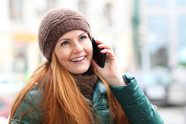 Mladý šťastný zrzavé vlasy žena volá telefonicky v jarní ulici — Stock fotografie