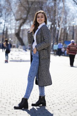 Gri bir ceket ve mavi kot esmer kız bahar parkında yürür