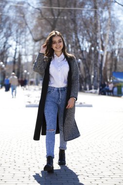 Gri bir ceket ve mavi kot esmer kız bahar parkında yürür