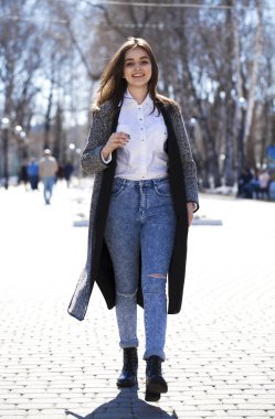 Gri bir ceket ve mavi kot esmer kız bahar parkında yürür