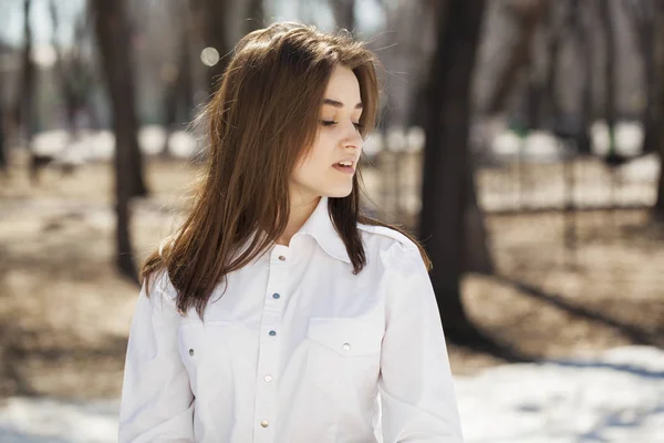 Jonge mooie brunette meisje in wit shirt poseren op de lente pa — Stockfoto