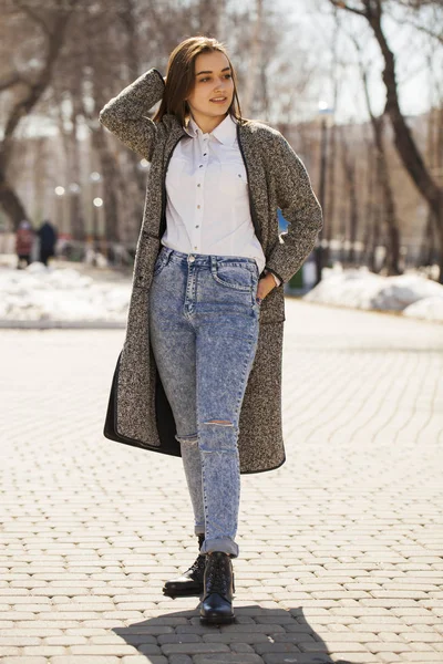 Брюнетка дівчина в сірому пальто і блакитні джинси гуляє в весняному парку — стокове фото