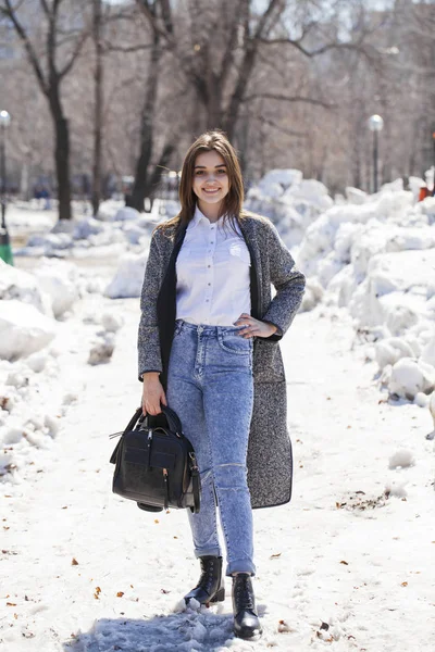 Brunetka dziewczyna w szarym płaszczu i niebieskie dżinsy spacery w parku wiosennym — Zdjęcie stockowe