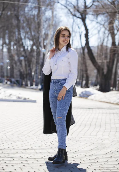 Девушка-подросток в белой рубашке и синих джинсах гуляет по весеннему парку — стоковое фото