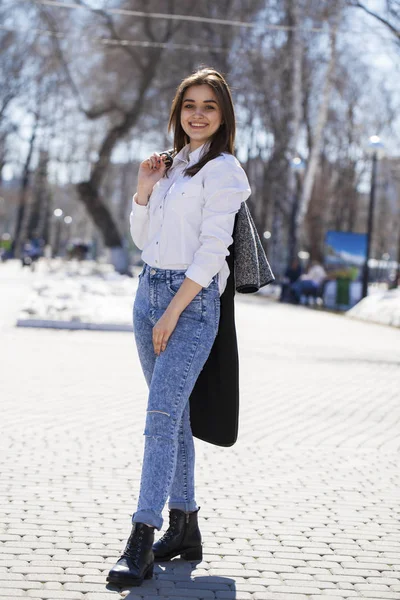 Teen girl in white shirt and blue jeans walks in spring park — Stock Photo, Image