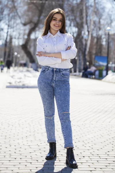 Девушка-подросток в белой рубашке и синих джинсах гуляет по весеннему парку — стоковое фото