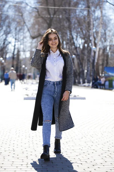 Bruna ragazza in un cappotto grigio e jeans blu passeggiate nel parco primaverile — Foto Stock