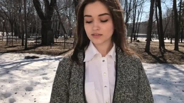 닫아. 젊은 아름 다운 갈색 머리 소녀 에 코트 포즈 에 봄 공원 — 비디오