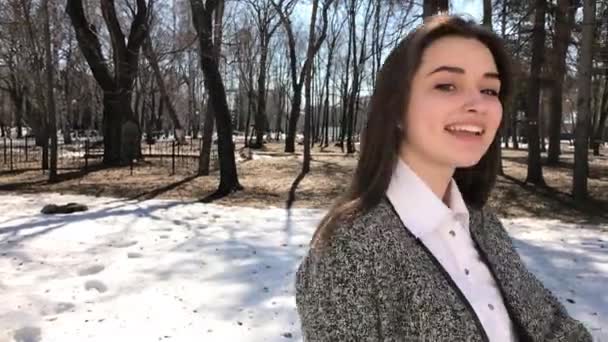 Chiudete. Giovane bella ragazza bruna in cappotto grigio in posa sul parco primaverile — Video Stock