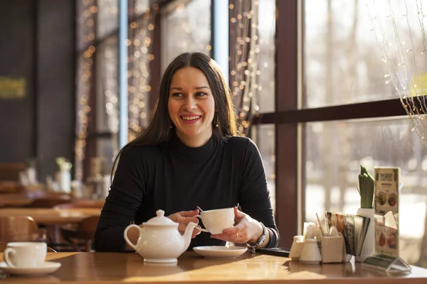 Jovem mulher bonita bebe chá sentado em um café contra o b — Fotografia de Stock