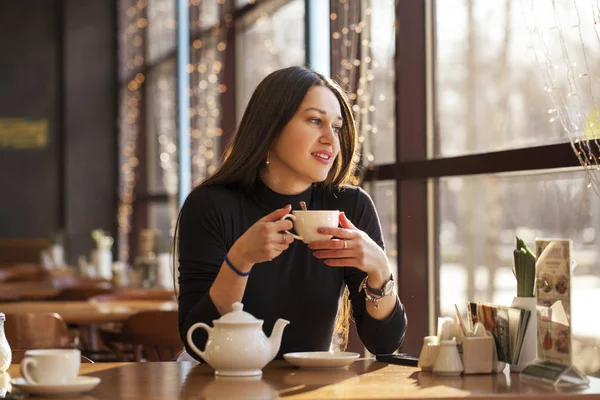 Young beautiful woman drinks tea sitting in a cafe against the b — Stock Photo, Image