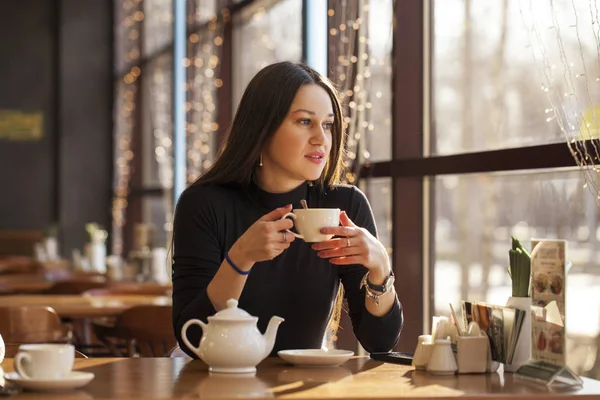 Jonge mooie vrouw drinkt thee zitten in een cafe tegen de b — Stockfoto