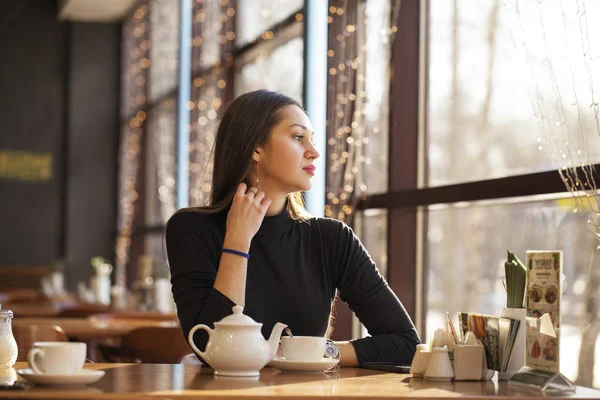 Молода красива жінка п'є чай, сидячи в кафе проти б — стокове фото