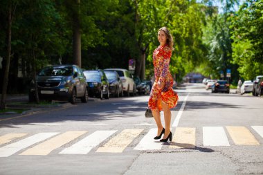 Kırmızı çiçekli elbisesi olan güzel sarışın kadın karşıya geçiyor.