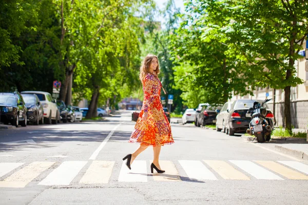 Junge schöne blonde Frau in einem roten Blumenkleid überquert das r — Stockfoto