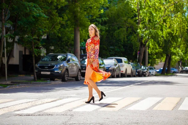 Ung vacker blond kvinna i en röd blomma klänning korsar r — Stockfoto