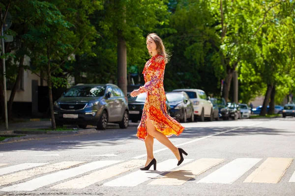 Junge schöne blonde Frau in einem roten Blumenkleid überquert das r — Stockfoto