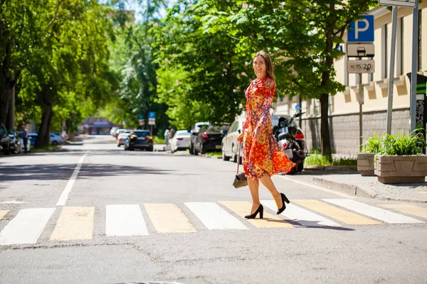 Young beautiful blonde woman in a red flower dress crosses the r — Stock Photo, Image