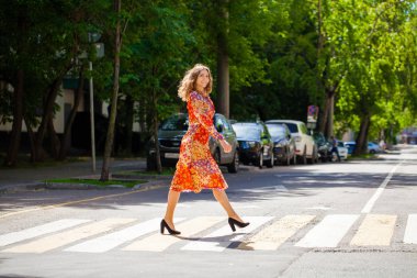 Kırmızı çiçekli elbisesi olan güzel sarışın kadın karşıya geçiyor.