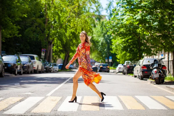 Young beautiful blonde woman in a red flower dress crosses the r — 스톡 사진