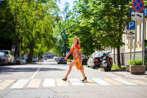 Junge schöne blonde Frau in einem roten Blumenkleid überquert das r — Stockfoto