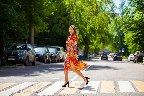 Young beautiful blonde woman in a red flower dress crosses the r — 스톡 사진