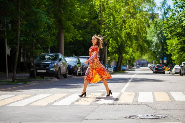 Young beautiful blonde woman in a red flower dress crosses the r — 스톡 사진