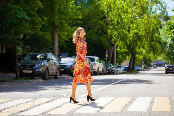 Junge schöne blonde Frau in einem roten Blumenkleid überquert das r — Stockfoto