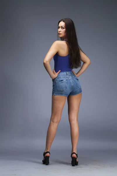 Mulher morena em roupa de banho azul e calções jeans posando em t — Fotografia de Stock