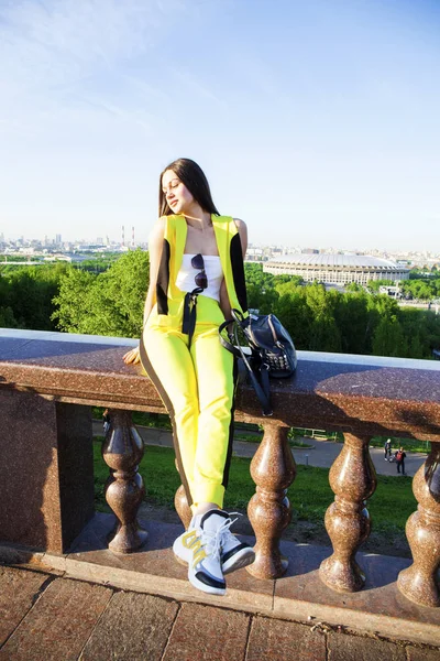 Hermosa mujer en un mono amarillo se sienta en la barandilla contra — Foto de Stock