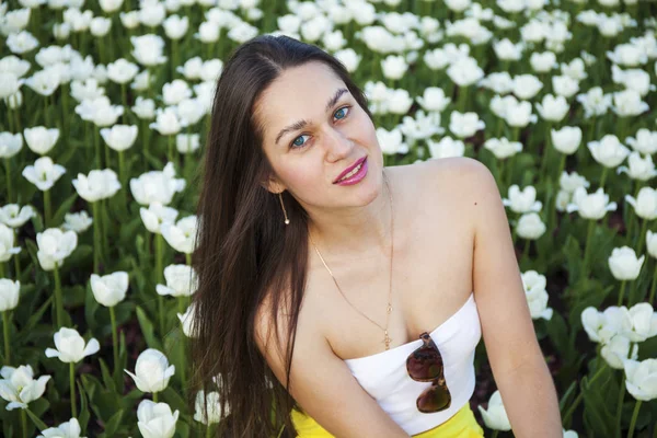 Junge brünette Frauen auf dem Hintergrund einer Lichtung von Tulpen fließen — Stockfoto