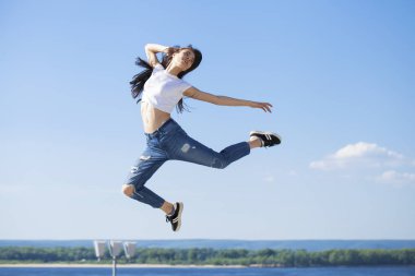 Genç güzel esmer kadın mavi gökyüzüne karşı poz veriyor.
