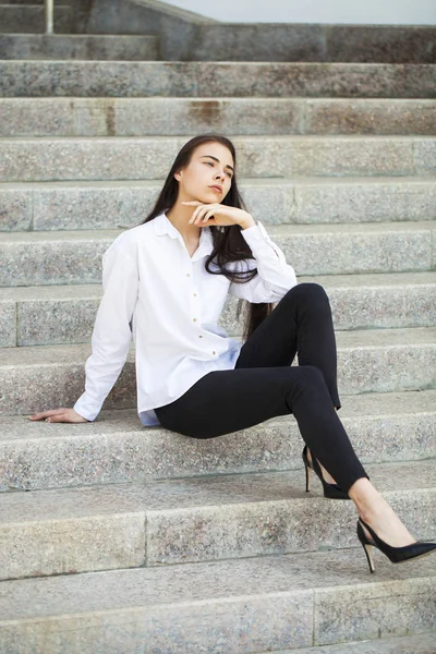 Mladá krásná brunetka v bílé košili, která sedí na kameni — Stock fotografie