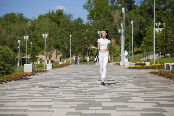 Junge schöne brünette Mädchen in weißen Jeans und T-Shirt zu Fuß — Stockfoto