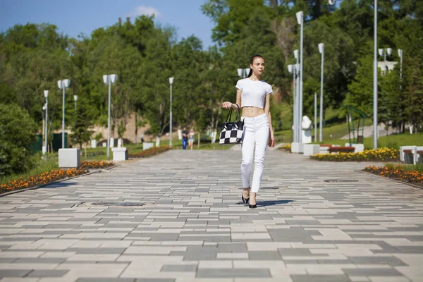 Junge schöne brünette Mädchen in weißen Jeans und T-Shirt zu Fuß — Stockfoto