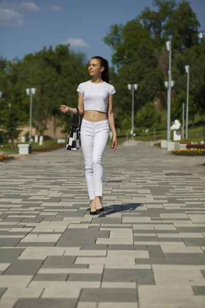 Joven hermosa chica morena en jeans blancos y camiseta caminando —  Fotos de Stock