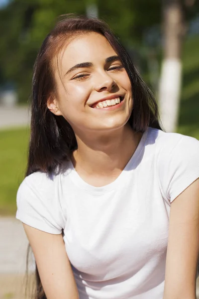 Beautiful brunette woman posing against summer park, bright sunn — Stock Photo, Image