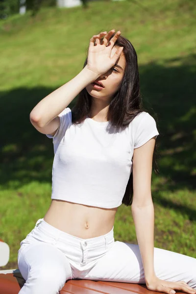 Hermosa mujer morena posando contra el parque de verano, sol brillante —  Fotos de Stock