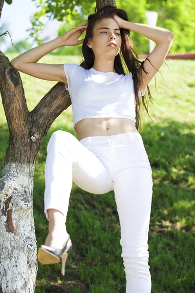 Hermosa mujer morena posando contra el parque de verano, sol brillante —  Fotos de Stock